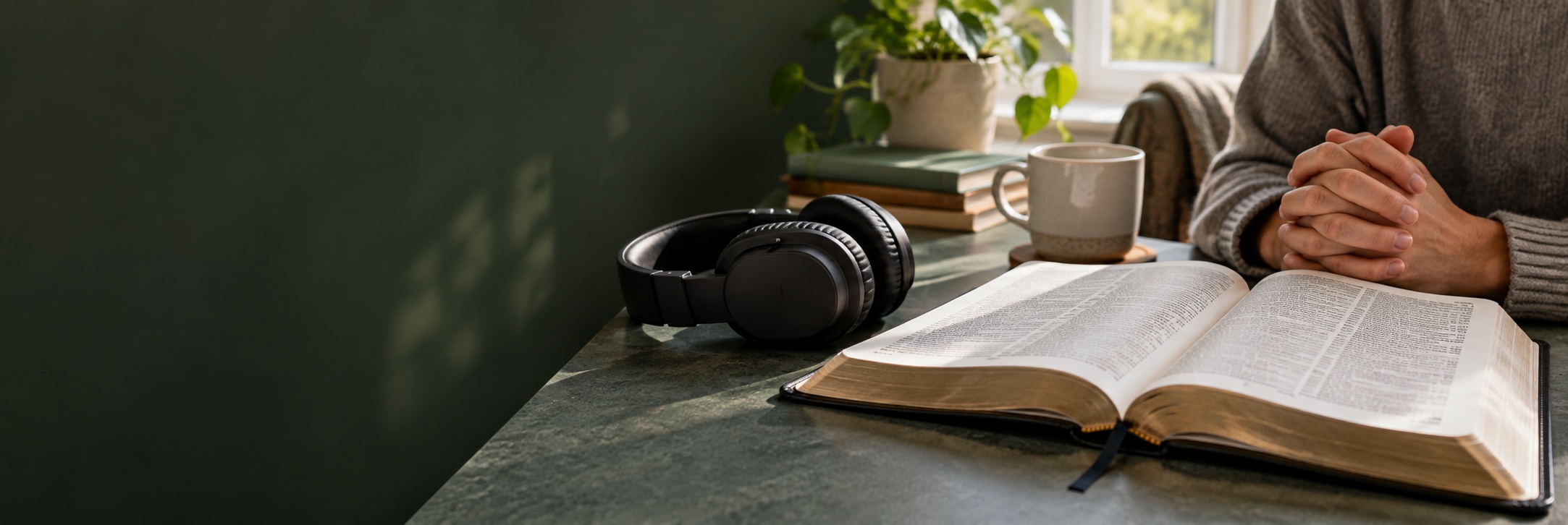 Headphones beside an open Bible, with hands clasped in prayer in a peaceful home.